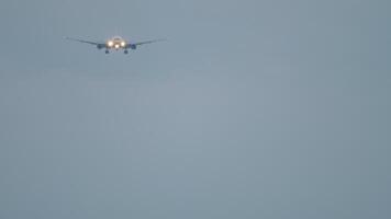 Long shot of a jet aircraft with an unrecognizable livery with headlights on approaching for landing in the sunset cloudy sky video