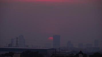 de zon is instelling over- een stad deken in mist, creëren een vaag en sfeervol tafereel. episch zonsondergang en stad mijlpaal gebouwen. rood en oranje zon reeks schemer Bij blauw lucht video