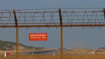 Airport fence with red Restricted Area sign. Jet plane with an unrecognizable livery taking off and climbing, front view, long shot video