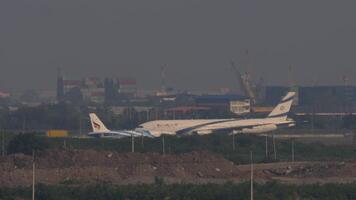 BANGKOK, THAILAND - MARCH 01, 2023. Long shot of a Boeing 777 of EL AL on the taxiway. Airbus A320 of Bangkok Air taxiing. Airfield at Suvarnabhumi Airport, Bangkok video