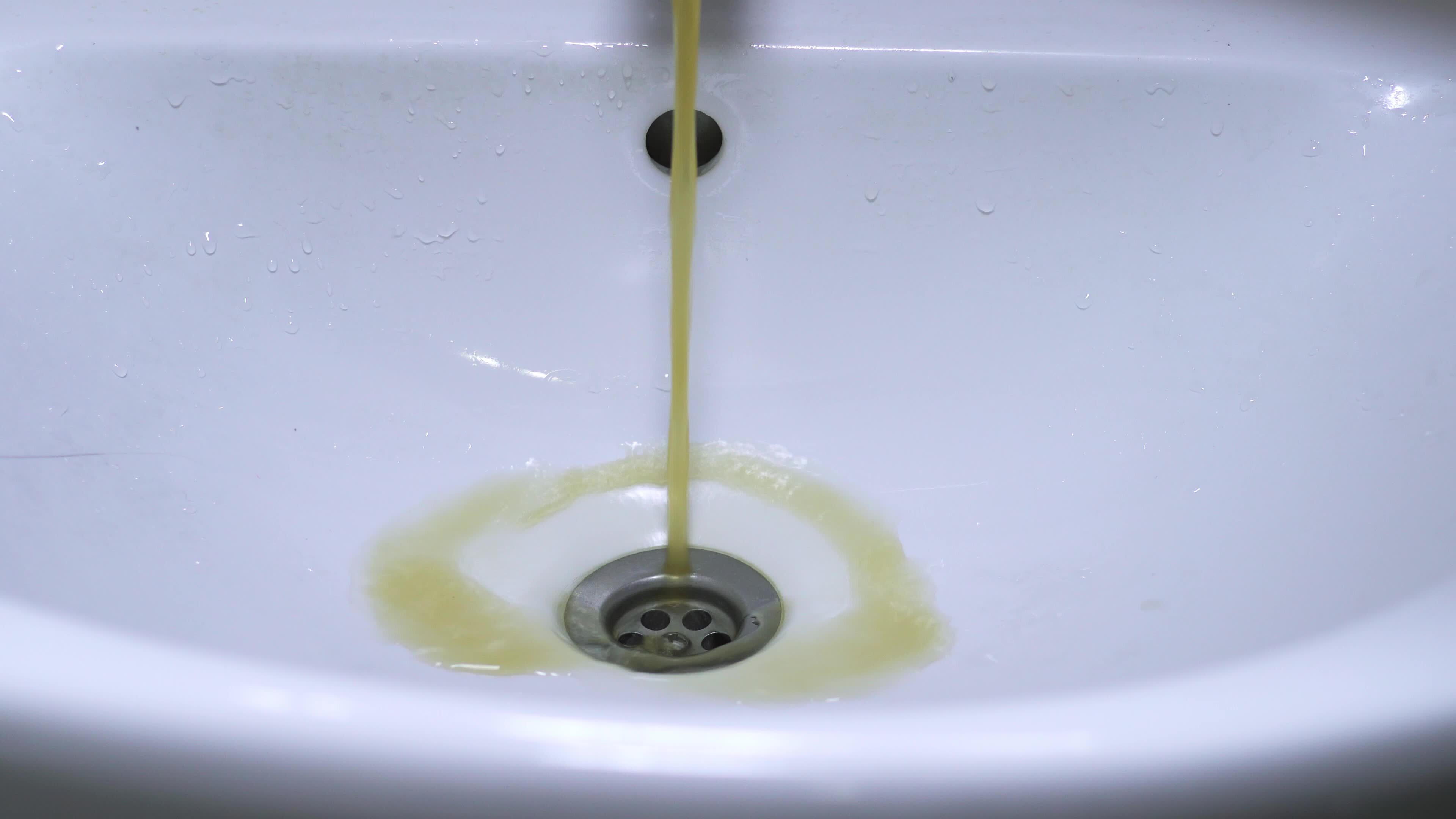 Dirty water flows from the tap. Yellow and brown tap water flows into the sink. Pollution of