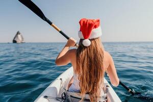 mujer en kayac espalda vista. contento joven mujer en Papa Noel sombrero flotante en kayac en calma mar. verano fiesta vacaciones y alegre hembra personas relajante teniendo divertido en el bote. foto