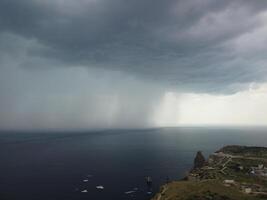 Aerial view footage of rain clouds over sea ocean Black clouds in bad weather day over sea surface High angle view nature view. Apocalypse. Storm Large freight dark gloomy rain clouds over a calm sea. photo