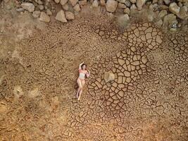 aéreo retrato de hermosa joven dama en bikini acostado en seco agrietado rojo suelo. árido, agrietado rojo suelo sequía y árido clima condiciones. clima y clima cambiar. foto