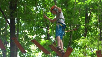 Rope park. A boy teenager in a helmet walks on suspended rope ladders. Carabiners and safety straps. Safety. Summer activity. Sport. Children's playground in nature in the forest video