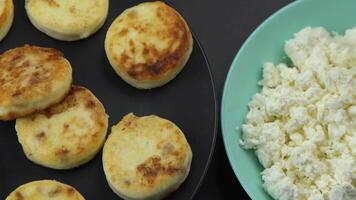 cheesecakes tillverkad från stuga ost och russin. förbereda mat för frukost. syrnik pannkakor. runda ost kaka på svart bakgrund. video