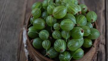 Green gooseberries in a wooden bowl. Harvest berries on a wooden table. Gooseberry summer vitamin food video