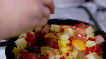 woman hand adding eggs to vegetable ragout with pieces of white bread frying on a frying pan with steam, closeup video