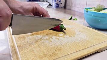 Caucasian hands cutting long red sweet pepper on bamboo cutting board at domestic kitchen, wide angle close-up with slow motion. video