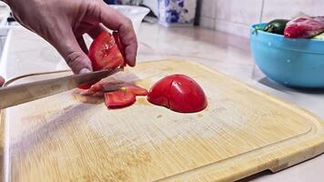 Caucasian hands cutting red tomato on bamboo cutting board at domestic kitchen, wide angle close-up with slow motion. video