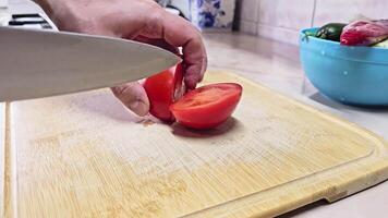 Caucasian hands cutting red tomato on bamboo cutting board at domestic kitchen, wide angle close-up with slow motion. video