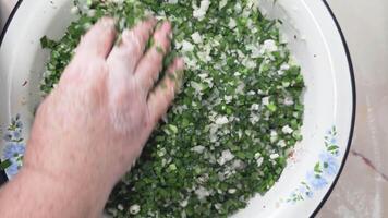 Senior Caucasian woman hands mix jusai and onions in an enamel basin in the kitchen, top view video