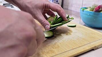 Caucasian hands cutting green cucumber on bamboo cutting board at domestic kitchen, wide angle close-up with slow motion. video