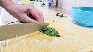 Caucasian hands cutting spinach leaves on bamboo cutting board at domestic kitchen, wide angle close-up with slow motion. video