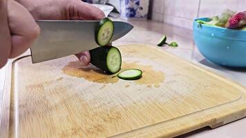 Caucasian hands cutting green cucumber on bamboo cutting board at domestic kitchen, wide angle close-up with slow motion. video