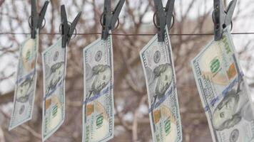 hundred US dollar bills hanging on string with clothespins and weaving on wind video