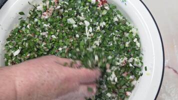 Senior Caucasian woman hands mix jusai and onions in an enamel basin in the kitchen, top view video