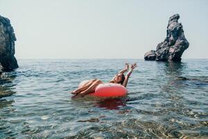 Woman summer sea. Happy woman swimming with inflatable donut on the beach in summer sunny day, surrounded by volcanic mountains. Summer vacation concept. photo