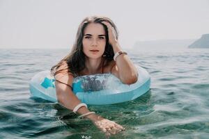 mujer verano mar. contento mujer nadando con inflable rosquilla en el playa en verano soleado día, rodeado por volcánico montañas. verano vacaciones concepto. foto