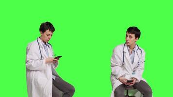 kvinna specialist använder sig av smartphone social media appar i studio, Sammanträde på en stol mot grönskärm bakgrund. läkare väntar för någon och bläddrar uppkopplad webbsidor, sms:a. kamera b. video