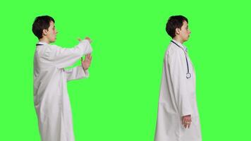 General practitioner doing timeout symbol and i dont know sign in studio, acting clueless and asking for a break against greenscreen backdrop. Woman medic wears white coat. Camera B. video