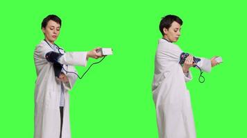 Healthcare specialist using a tonometer to measure high blood pressure and pulse, presenting tool used at checkup examinations. Doctor in white coat stands against greenscreen backdrop. Camera B. video