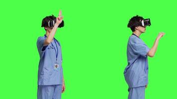 Medical assistant examining checkup results with virtual reality glasses, looking at 3d interactive lens against greenscreen. Nurse using vr headset in studio, find diagnosis for patients. Camera B. video