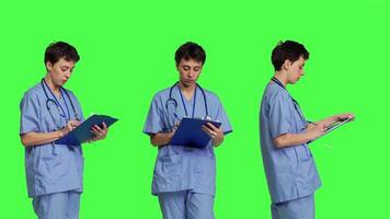 confidente hospital enfermero tomando notas para el siguiente médico cita, en pie terminado pantalla verde fondo. médico asistente con uniforme escritura paciente información en portapapeles documentos. cámara b. video