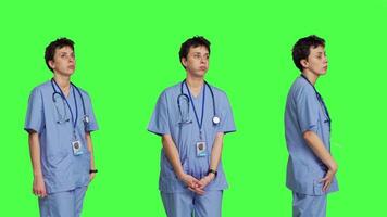 Stressed nurse checking time on watch and waiting for patient to arrive at checkup examination, being impatient against greenscreen backdrop. Medical assistant with scrubs and stethoscope. Camera B. video