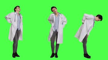 Woman physician experiencing lower back acute pain in studio, suffering from scoliosis and having muscles discomfort. Medic dealing with backache from burnout, greenscreen backdrop. Camera A. video