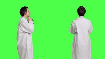 mulher médico é usando uma estetoscópio para ouço para respiração dentro estúdio, vestindo uma branco hospital casaco contra tela verde pano de fundo. médico com profissional perícia faz consultas. Câmera b. video