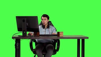 Woman player participating in online e sport tournament on computer, sitting at desk against greenscreen backdrop. Focused gamer playing video games shooter competition, leisure. Camera B.