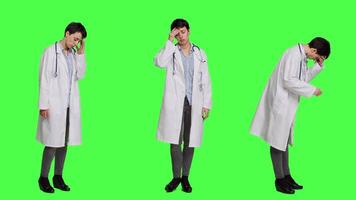 Unhappy medic dealing with a painful migraine against greenscreen backdrop, working in healthcare industry under pressure. Woman physician suffering from a headache, overworked. Camera A. video