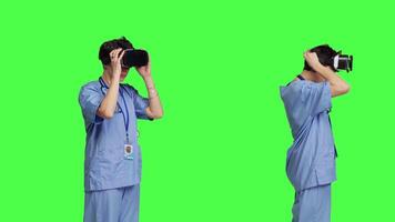 Medical assistant working with virtual reality glasses against greenscreen backdrop, using interactive 3d vision on vr headset to do checkup examination. Young nurse uses modern gadget. Camera B. video