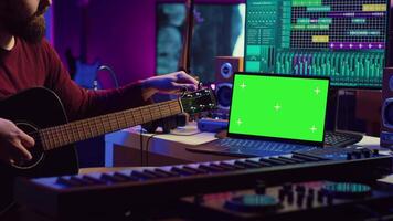 musicus aan het leren naar Speel nieuw akoestisch instrument in zijn huis studio, beoefenen online gitaar lessen Aan geïsoleerd groene scherm Scherm. aan het kijken zelfstudie Aan laptop naar ontwikkelen zijn vaardigheden. camera a. video