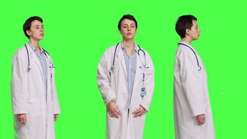 Porträt von Gesundheit Spezialist tragen ein Weiß Krankenhaus Mantel im Studio, Stehen gegen grüner Bildschirm Hintergrund. erfolgreich Arzt posieren mit Vertrauen, medizinisch Industrie Sachverstand. Kamera b. video