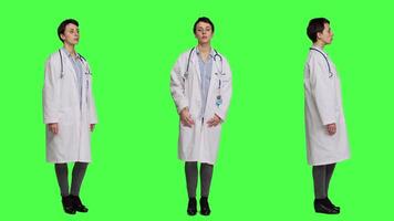 Porträt von Gesundheit Spezialist tragen ein Weiß Krankenhaus Mantel im Studio, Stehen gegen grüner Bildschirm Hintergrund. erfolgreich Arzt posieren mit Vertrauen, medizinisch Industrie Sachverstand. Kamera a. video