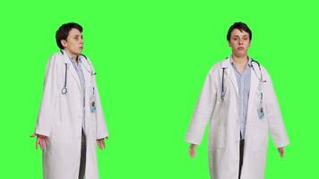 Physician being uncertain about something in studio, shrugging and feeling clueless about the right answer. Doctor doing i dont know symbol against greenscreen backdrop, confusion. Camera B. video