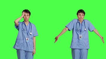 Medical assistant having a headache and doing confusion symbol, standing against greenscreen backdrop. Nurse deals with a migraine and burnout, shows i dont know sign and being clueless. Camera B. video