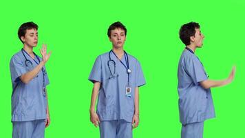 Health specialist with blue scrubs showing stop sign in studio, standing against greenscreen backdrop. Nurse expressing denial and refusal with warning forbidden symbol, denying something. Camera B. video