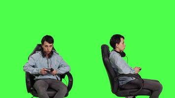 Happy gamer winning an online shooter competition in studio, playing e sport tournament against greenscreen backdrop. Young woman player celebrating her gaming victory on chair. Camera B. video