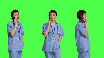 Health specialist using smartphone to make important calls, standing against greenscreen backdrop. Nurse talking to patients for checkup exams on telephone line, calling people to confirm. Camera B. video