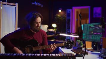 Portrait of artist recording tunes on daw software with his guitar, enjoying time in his home studio office. Audio engineer and musician creating new tracks, stereo electronic instruments. Camera B. video