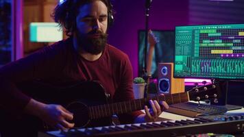 Musical composer recording his guitar tunes and adding piano key sounds, creating a beautiful song with mixing console and daw software. Sound engineer working with electronic tools. Camera B. video