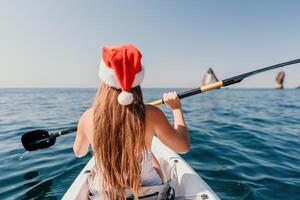 mujer en kayac espalda vista. contento joven mujer en Papa Noel sombrero flotante en kayac en calma mar. verano fiesta vacaciones y alegre hembra personas relajante teniendo divertido en el bote. foto