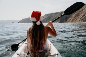 mujer en kayac espalda vista. contento joven mujer en Papa Noel sombrero flotante en kayac en calma mar. verano fiesta vacaciones y alegre hembra personas relajante teniendo divertido en el bote. foto