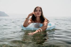 mujer verano mar. contento mujer nadando con inflable rosquilla en el playa en verano soleado día, rodeado por volcánico montañas. verano vacaciones concepto. foto