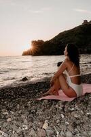 Woman sea yoga. Happy woman meditating in yoga pose on sunset beach, ocean and rock mountains. Motivation and inspirational fit and exercising. Healthy lifestyle outdoors in nature, fitness concept. photo