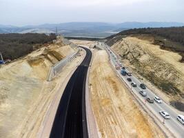 Mountain road constraction. Workers reinforce the slope over the new road. Road construction in progress on slope nature canyon. Infrastructure development and logistics. Aerial drone shot photo