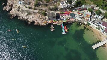 Aerial drone view on colorful kayaks grouped at a dock in sea bay. Group of happy kayakers are walking or training with instructor at sea bay. Active sea vacations concept video